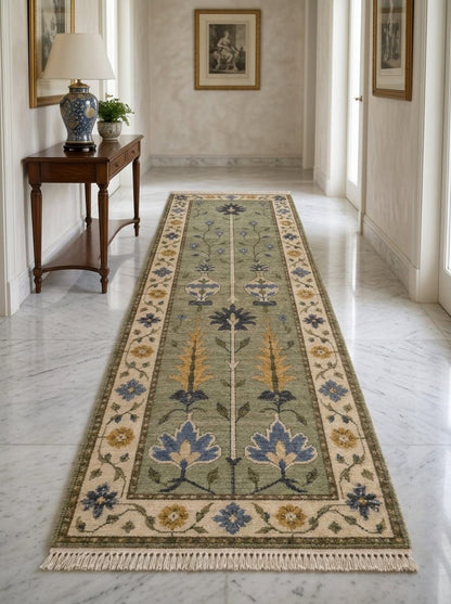 Hand Knotted Oushak Runner Rug in sage green wool, with ivory floral border, blue and mustard motifs, and fringed ends.