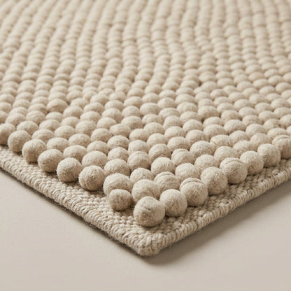 Chunky Wool Rug in oatmeal beige, with a thick handwoven surface of raised rounded pebble rows and braided edges.