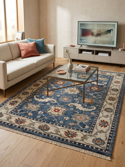 Oushak Hand Knotted Rug in blue wool, with ivory floral border, scrolling leaf motifs, rust and sage flowers, and fringed ends.