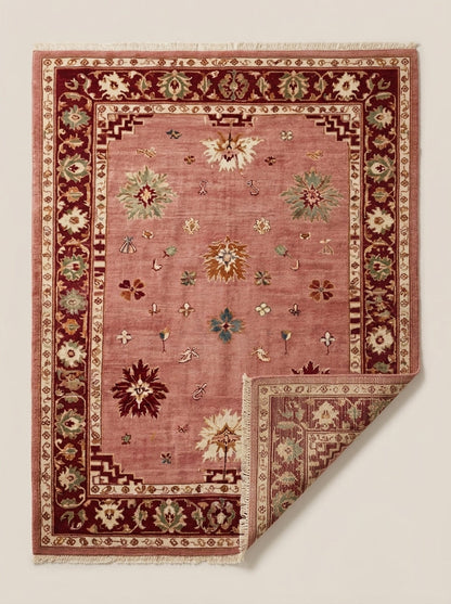Oushak Hand Knotted Rug in dusty rose wool, featuring scattered floral motifs, stepped corners and a burgundy floral border.