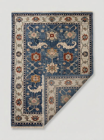Oushak Hand Knotted Rug in blue wool, with ivory floral border, scrolling motifs, rust and gold flowers, and fringed ends.