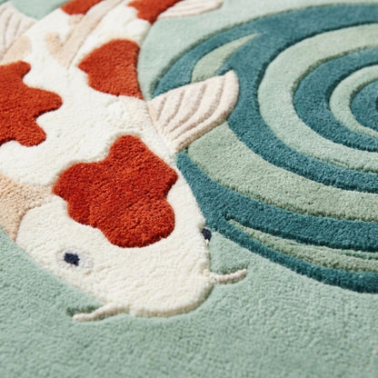 Round Koi Fish Rug in plush wool, showing a white koi with orange patches beside carved teal and sage ripple rings