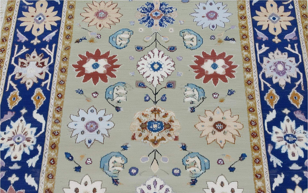 Top view of sage green floral area rug with navy border and intricate traditional Oushak design
