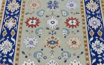 Top view of sage green floral area rug with navy border and intricate traditional Oushak design