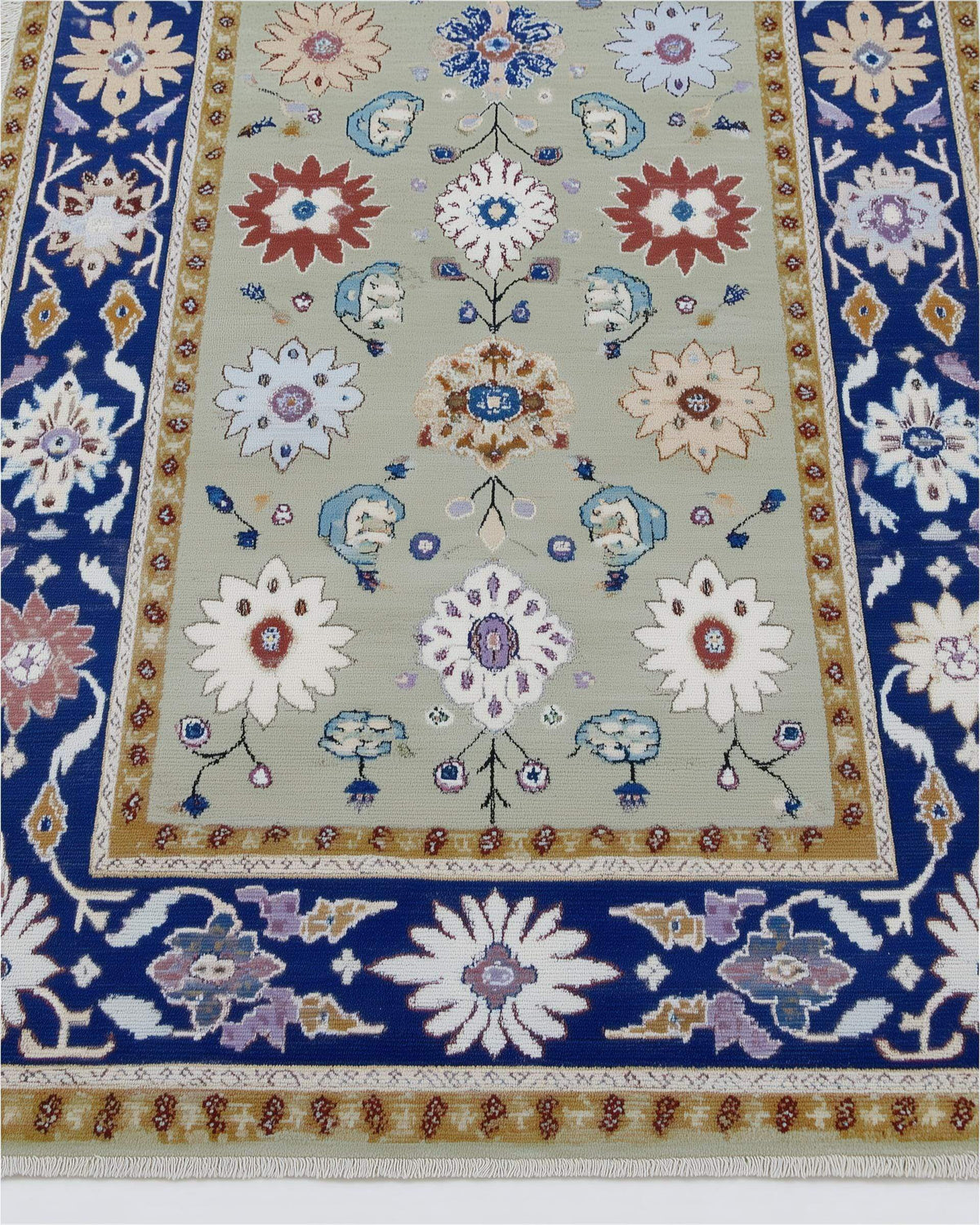Sage green floral area rug with traditional Oushak design, navy border, and botanical motifs on stone floor.
