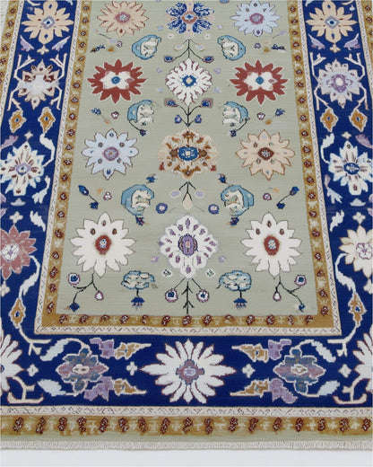 Sage green floral area rug with traditional Oushak design, navy border, and botanical motifs on stone floor.