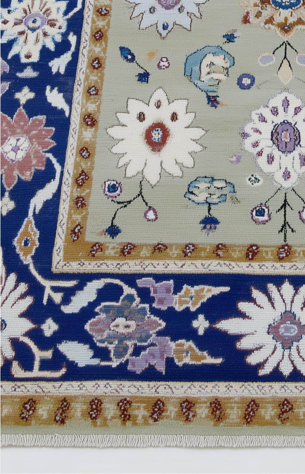 Top view of sage green floral area rug with navy border and traditional Oushak design on stone floor