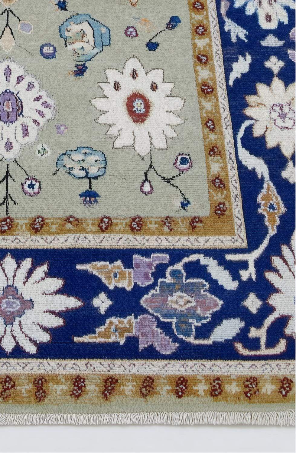 Sage green floral area rug with traditional Oushak design and navy border on stone floor