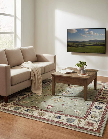 Hand-tufted sage green Oushak rug with floral and vine patterns in muted terracotta, navy, and cream colors