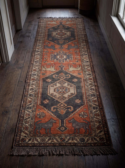 Vintage tribal runner rug with geometric medallions and animal motifs in rust orange and charcoal gray, hand-knotted wool Persian-style hallway carpet.